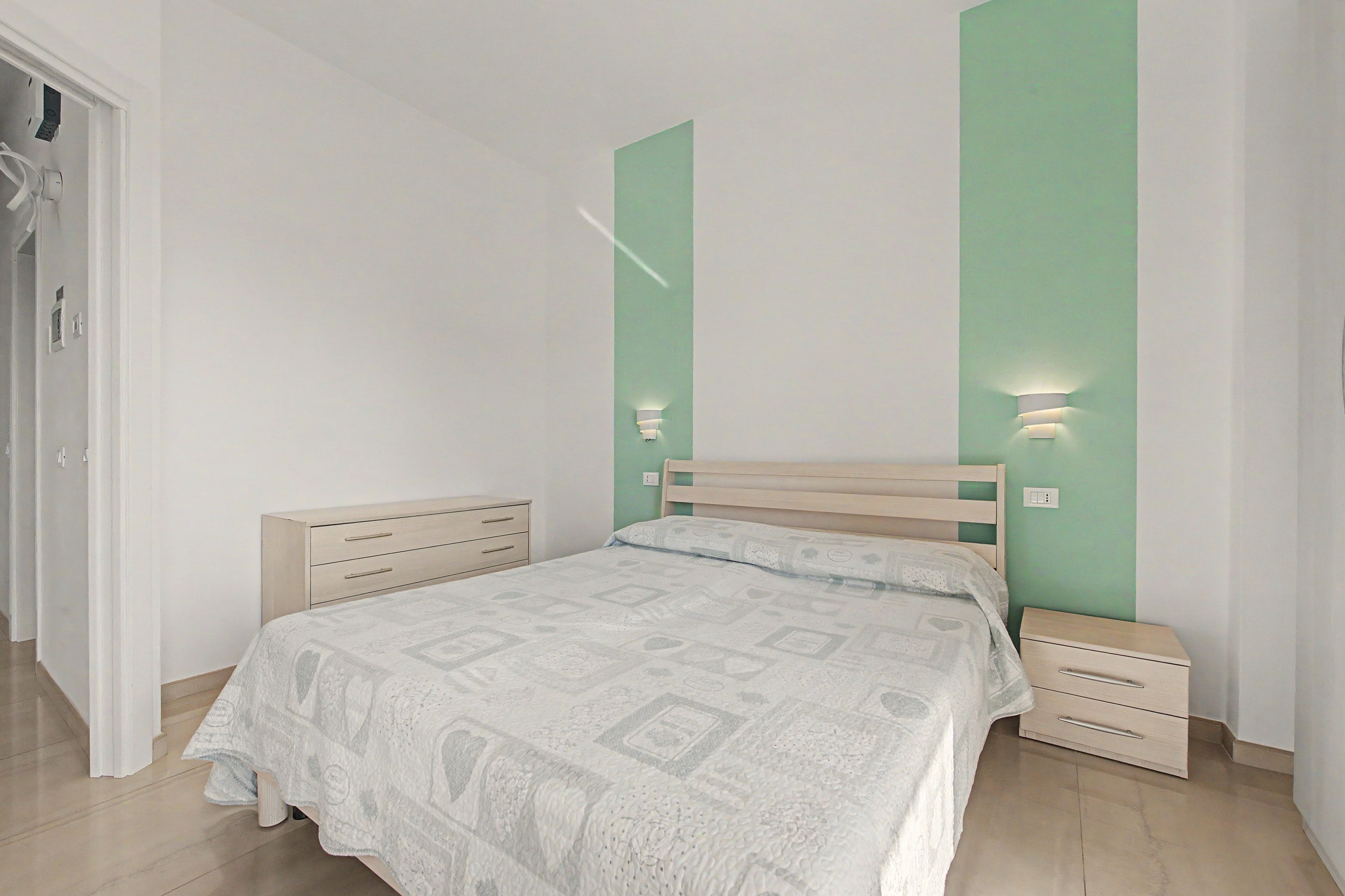 Ein Schlafzimmer mit einem Bett, Nachttischen, einem Kleiderschrank und einer Wand in Grünton.