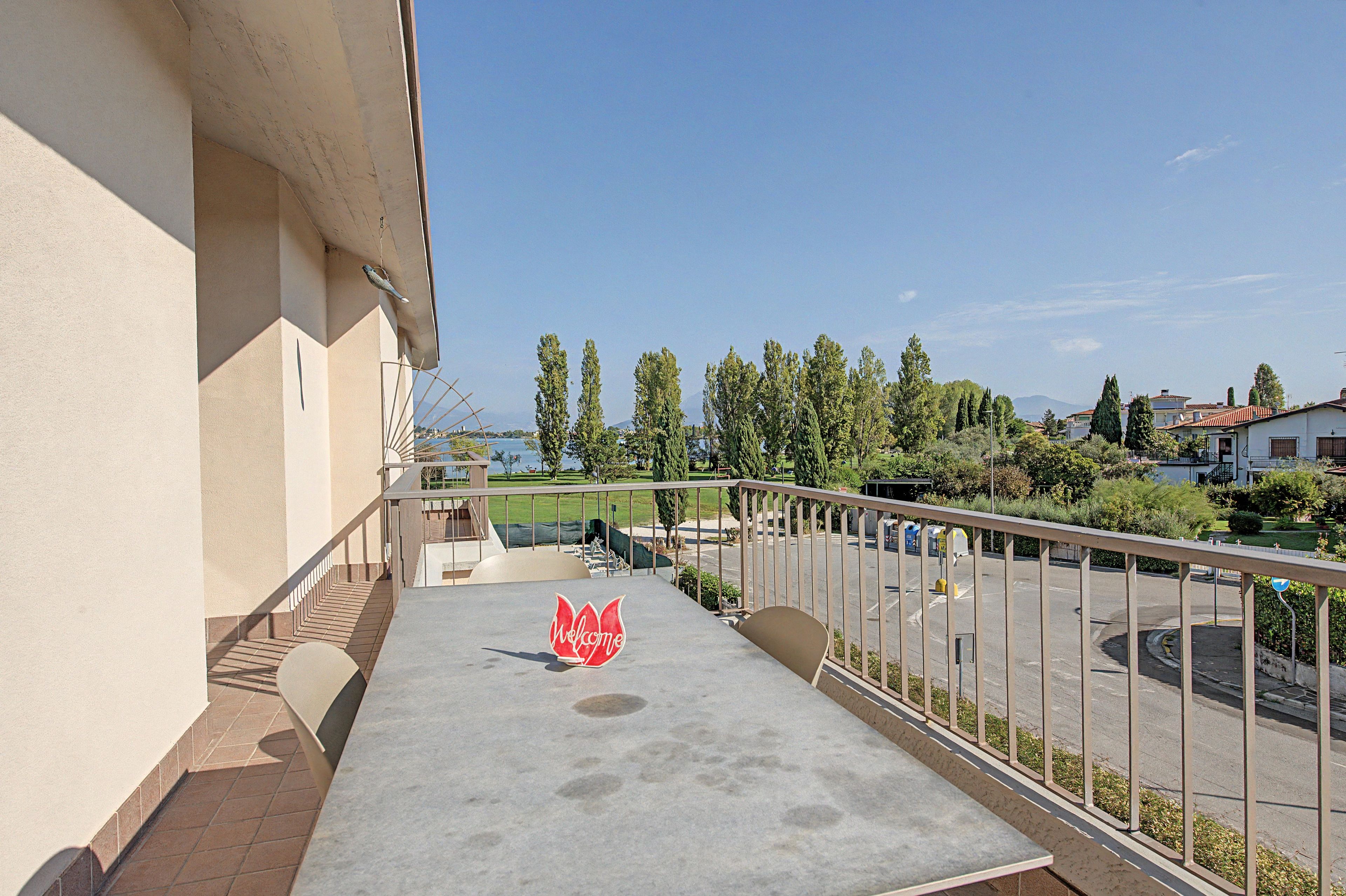 Ein Balkon mit einem Willkommensschild, Blick auf eine Grünfläche mit Bäumen und einem klaren Himmel.