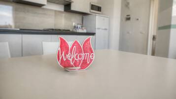 A red and white paper welcome sign on a table in a modern kitchen with white cabinets and a microwave.