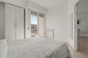 Ein Schlafzimmer mit Bett, Schrank, Heizkörper und einer offenen Tür, die auf einen Balkon führt.