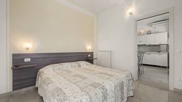 Una camera da letto con un letto, comodini, termosifone e vista su una zona cucina.