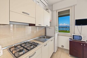 A modern kitchen with a gas stove, a built-in oven, a sink, and a window with a view of a lake and mountains. - Peonia Apartment – Lake View Three-Room with Lake View, Wi-Fi, and Air Conditioning (Sirmione)