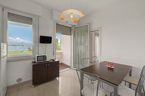 A modern room with a dining table, chairs, a television, and a view of the sea. - Peonia Apartment – Lake View Three-Room with Lake View, Wi-Fi, and Air Conditioning (Sirmione)
