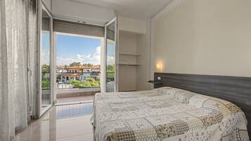 A bedroom with a large bed, a sliding glass door to a balcony, and a view of a residential area.