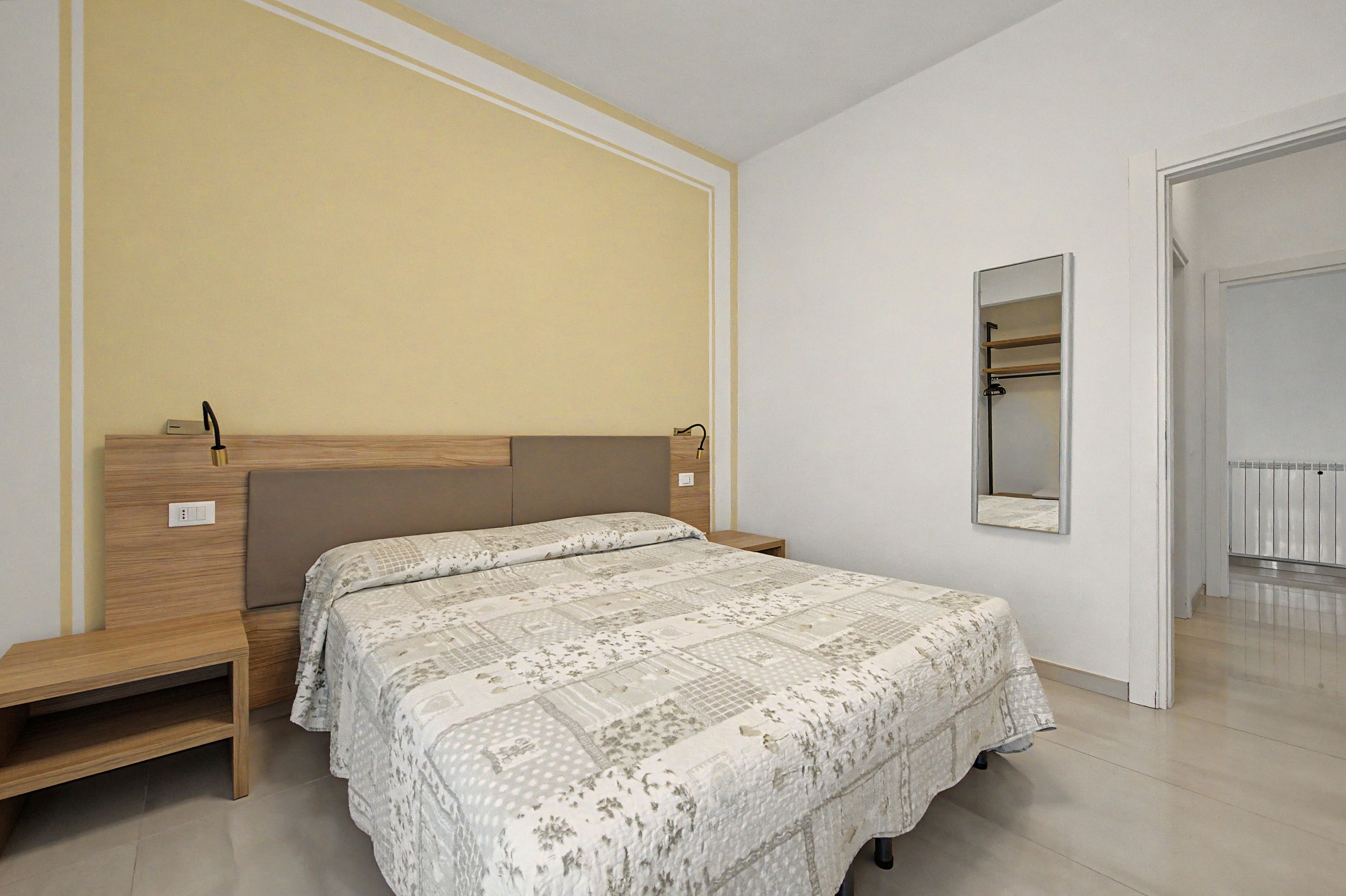 Un dormitorio con cama, mesitas de noche, armario y espejo.