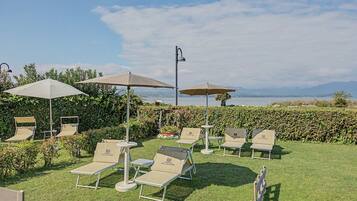 Eine Terrasse mit Sitzgelegenheiten und Sonnenschirmen mit Blick auf ein Gewässer und entfernte Berge.