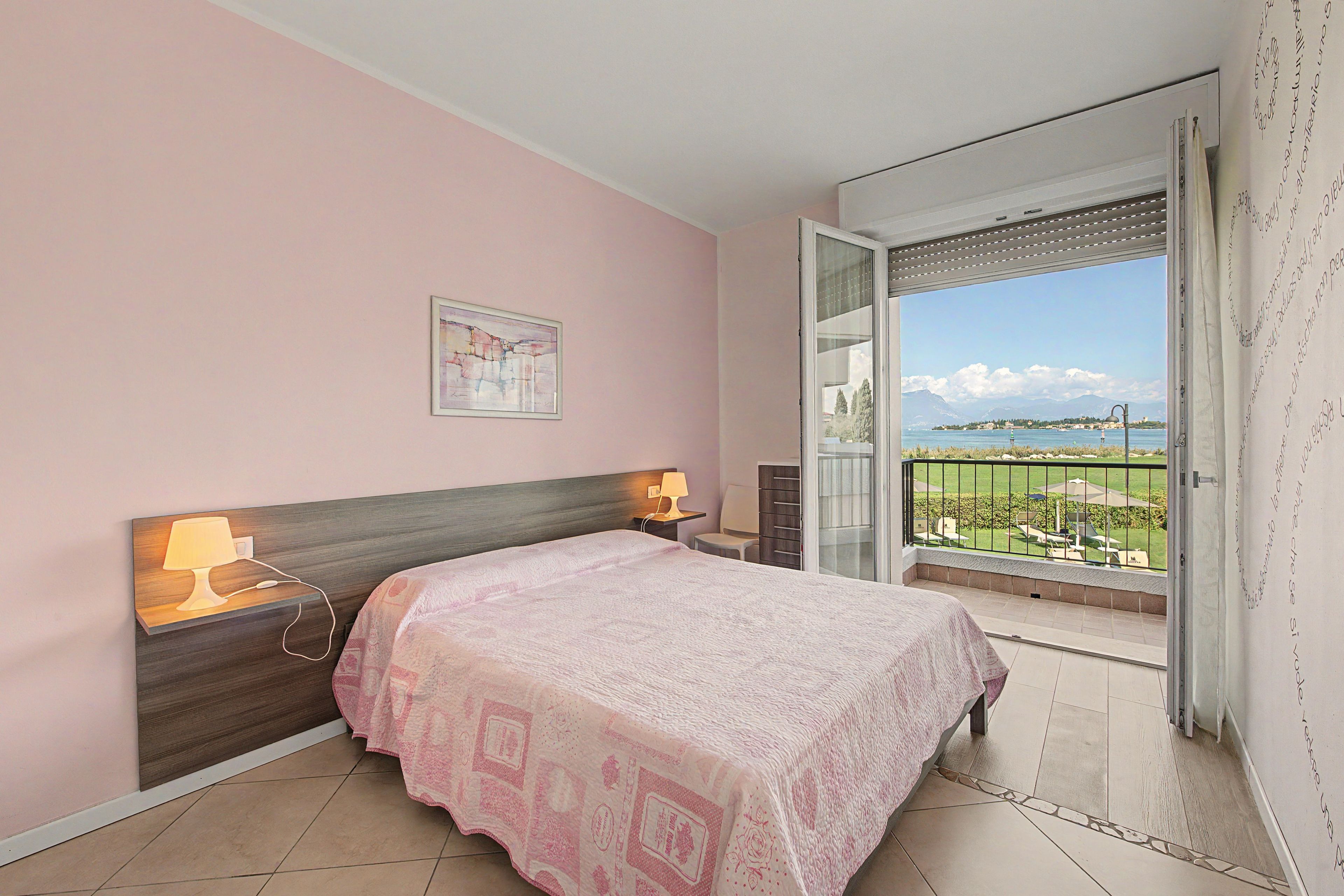 Ein Schlafzimmer mit einem Bett, Nachttischlampen, einem Gemälde und einem Balkon mit Blick.