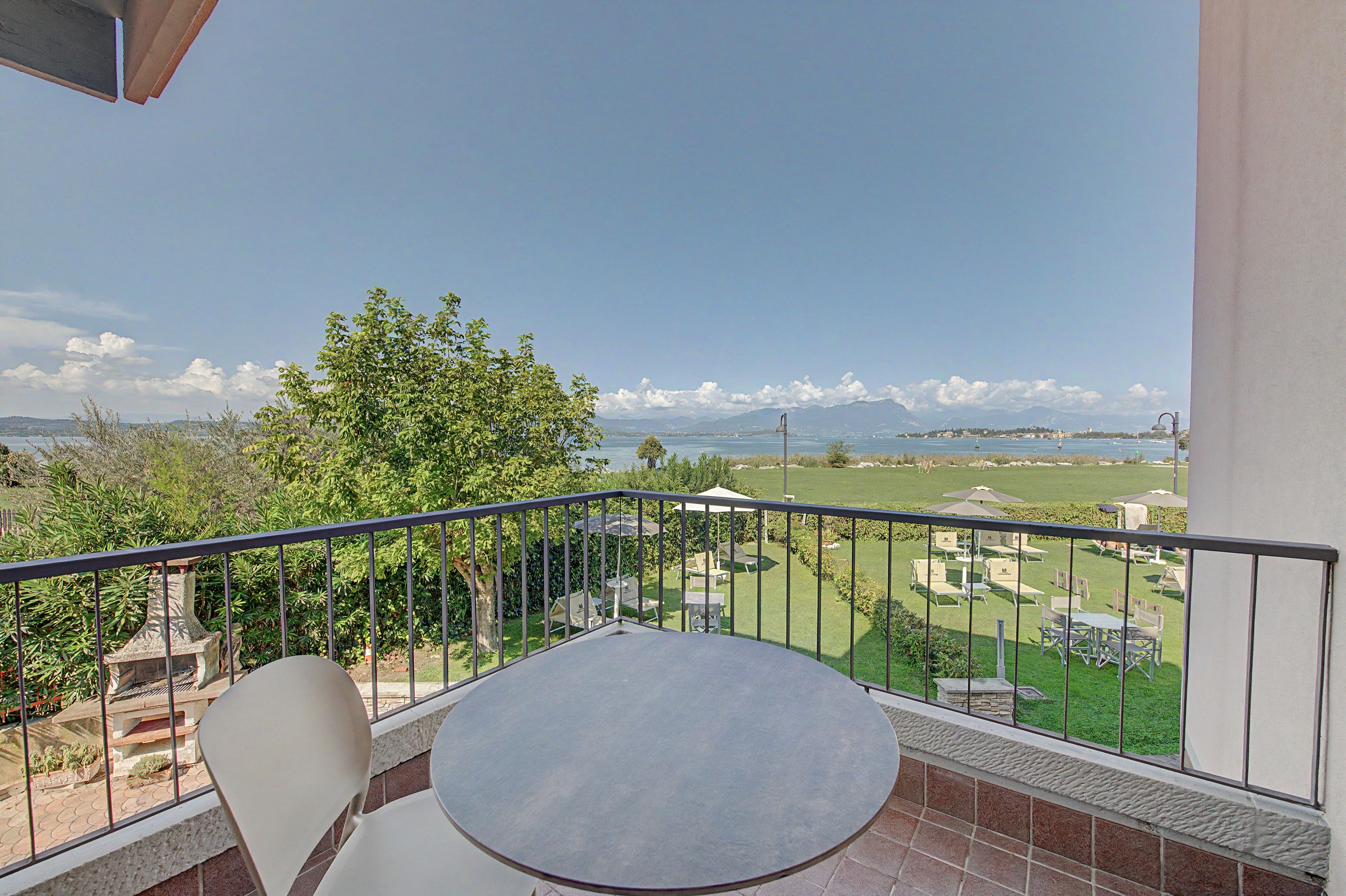 Un balcone con tavolo e sedie, vista su uno specchio d'acqua e un paesaggio lontano.