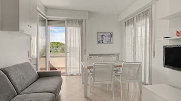 Un soggiorno moderno con un divano grigio, un tavolo da pranzo con sedie, una TV e un balcone con vista sul verde.