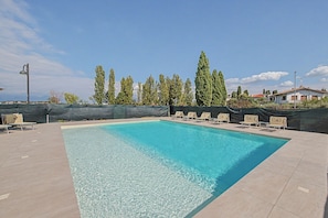 A swimming pool with clear water, surrounded by lounge chairs and a row of tall trees. - Viola Apartment - Lake View Two-Room with WiFi, Air Conditioning, and Lake View (Sirmione)