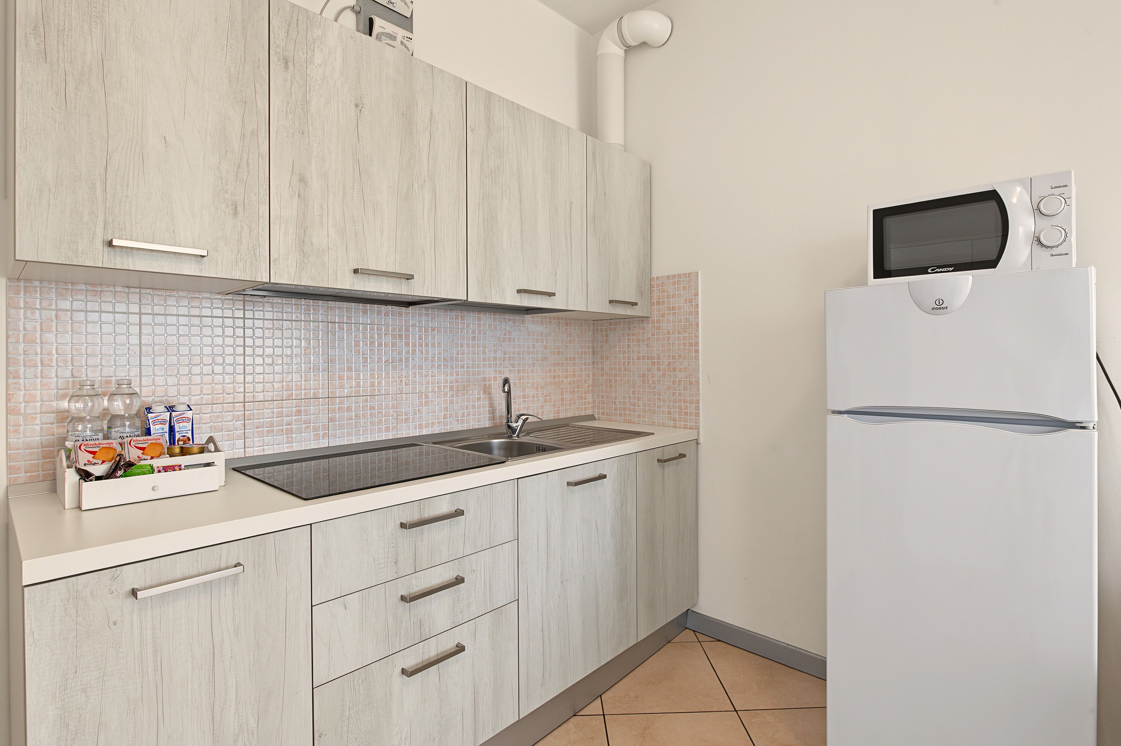 A kitchen with a white refrigerator, a microwave, and a sink with a tiled backsplash.