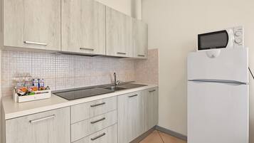 A kitchen with a white refrigerator, a microwave, and a sink with a tiled backsplash.