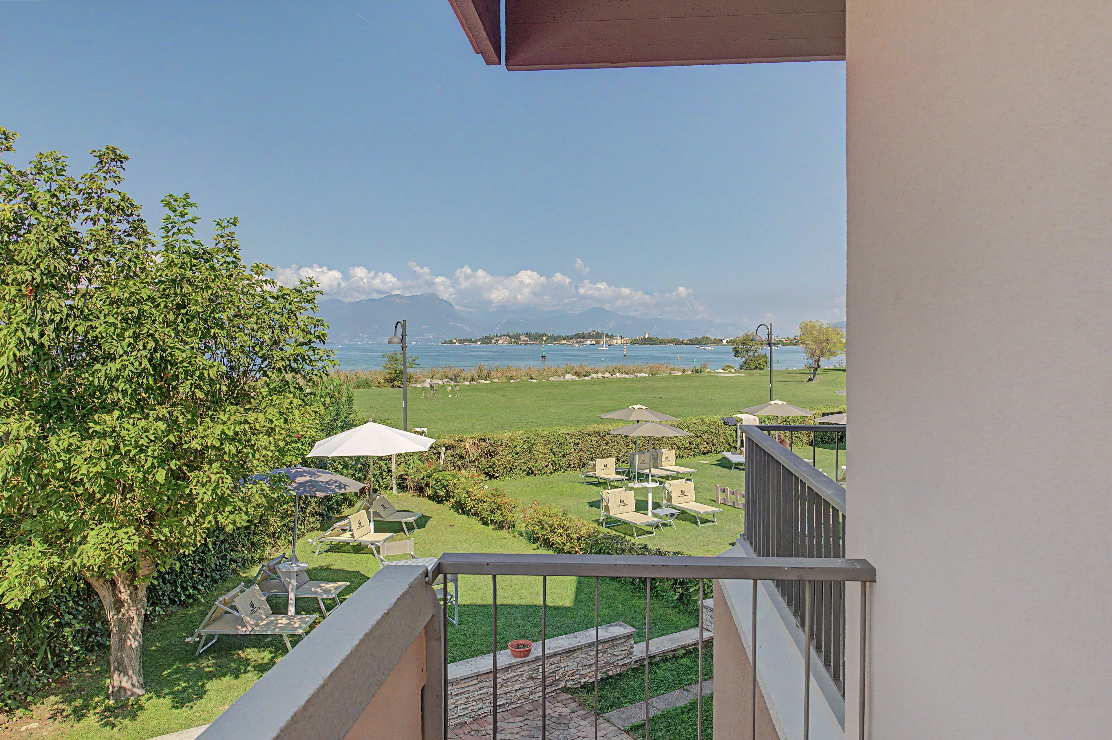 Ein Balkon mit Blick auf einen angelegten Garten, Sitzgelegenheiten im Freien und ein weiter See in der Ferne.
