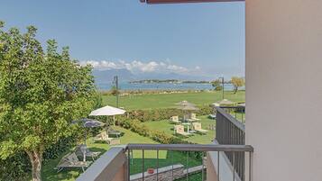 Ein Balkon mit Blick auf einen angelegten Garten, Sitzgelegenheiten im Freien und ein weiter See in der Ferne.