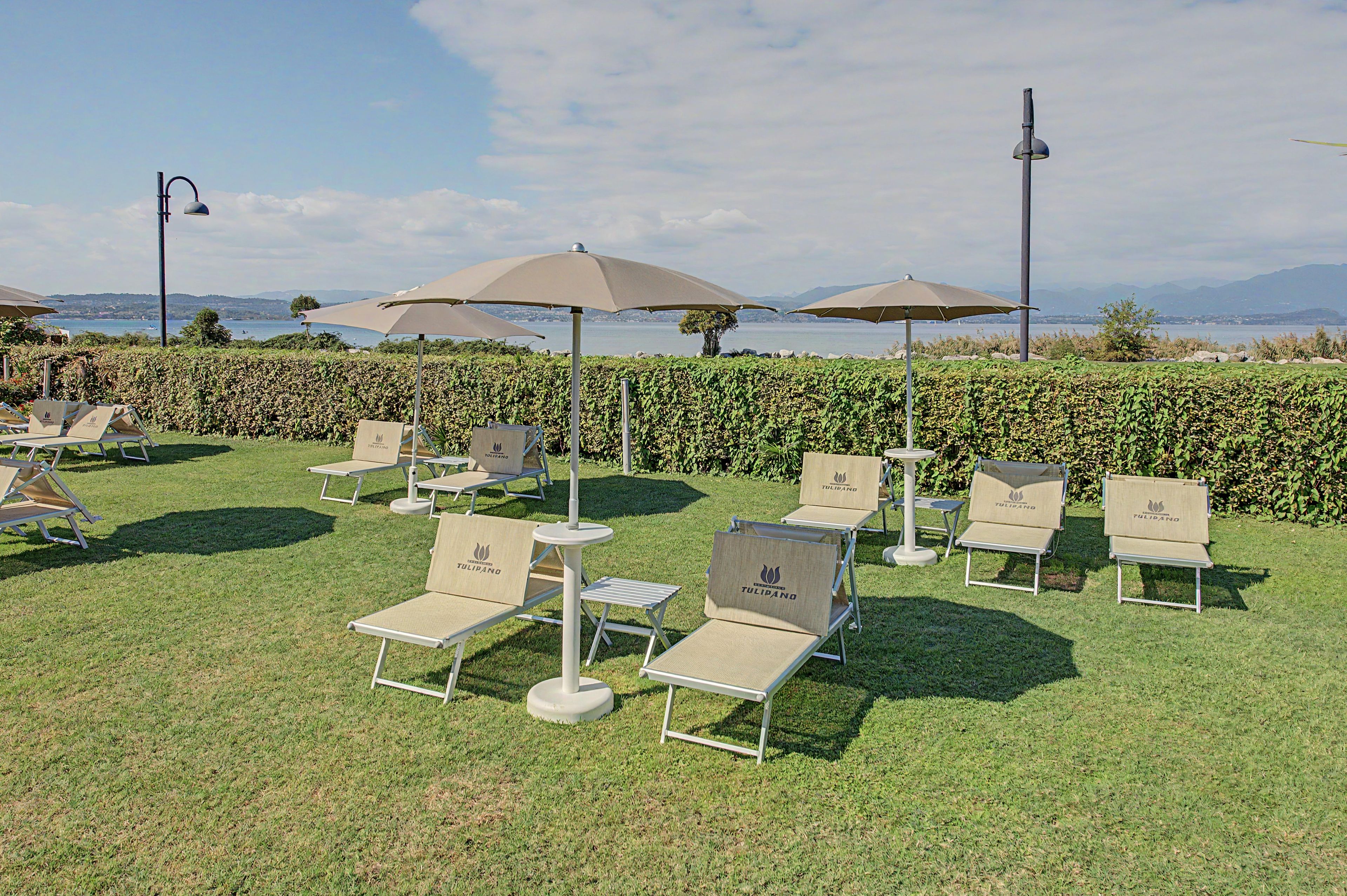 Eine Terrasse mit Gartenmöbeln und Sonnenschirmen mit Blick auf ein Gewässer.