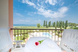 A balcony with a white table, a red rose, and a view of a pool and greenery. - Peonia Apartment - Lake View Two-Room with Lake View, Wi-Fi, and Air Conditioning (Sirmione)