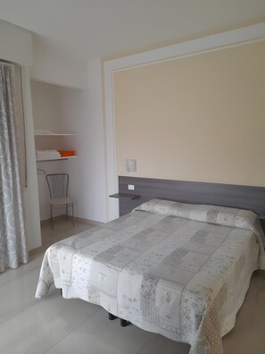 Quarto de hotel com cama, uma cadeira, escrivaninha e cortina.