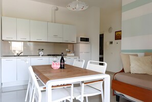 A modern kitchen with white cabinets, a wooden dining table, and a microwave. - Papavero Apartment - Lake View Three-Room with Wi-Fi and Air Conditioning (Sirmione)