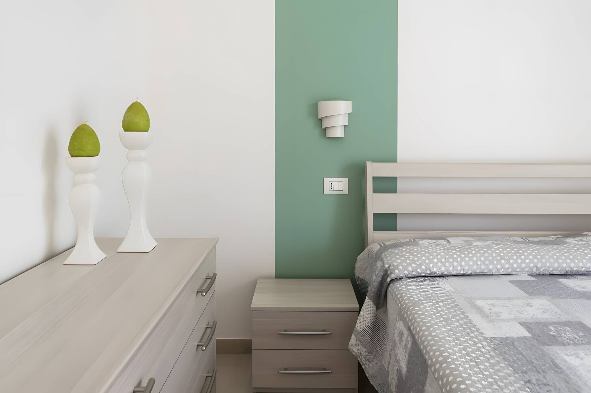 Ein Schlafzimmer mit Bett, Nachttisch, Lampe und einer Kommode mit zwei Dekorationen.