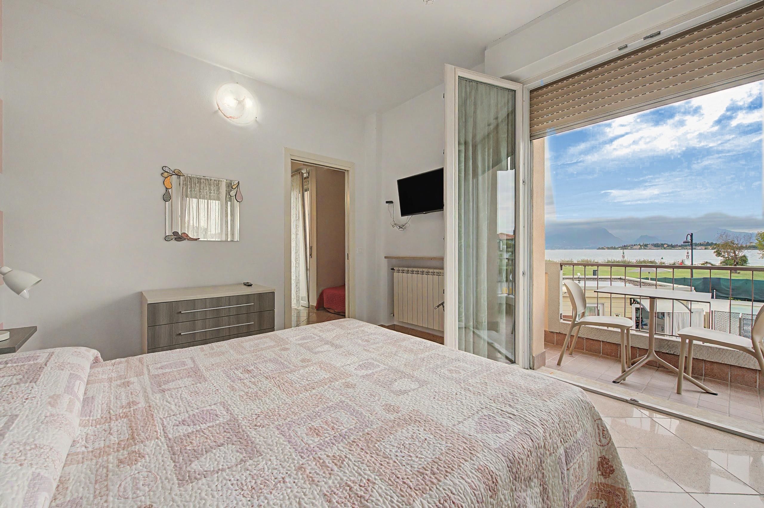 Un dormitorio con cama, cómoda, televisor y un balcón con vistas.