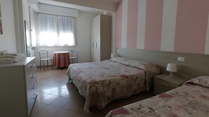 Ein Schlafzimmer mit zwei Betten, einem Schreibtisch, einem Stuhl, einem Fenster mit Vorhängen und einer gestreiften Wand.