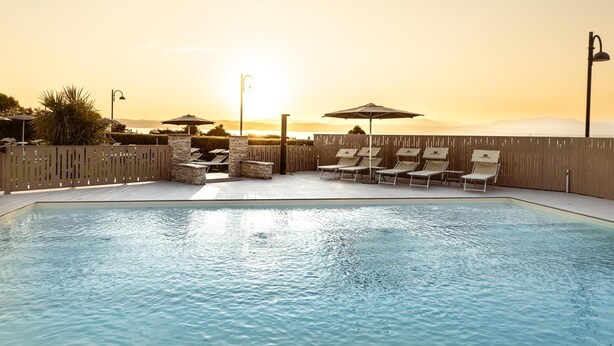 Ein Swimmingpool mit Liegestühlen und Sonnenschirmen, umgeben von einem Holzzaun, bei Sonnenuntergang.