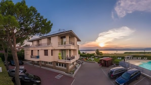 Ein mehrstöckiges Gebäude mit Balkonen, einem Swimmingpool und Blick auf den Sonnenuntergang über dem Wasser.