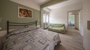 Ein Schlafzimmer mit einem Bett, einem grünen Sofa, einem Bild an der Wand und Blick in einen weiteren Raum.