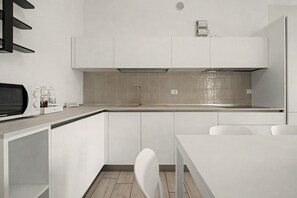 A modern kitchen with white cabinetry, a built-in microwave, and a small dining area with a white table and chair. - 'Calla - Trilocale Deluxe' Apartment with Lake View, Wi-Fi and Air Conditioning (Sirmione)
