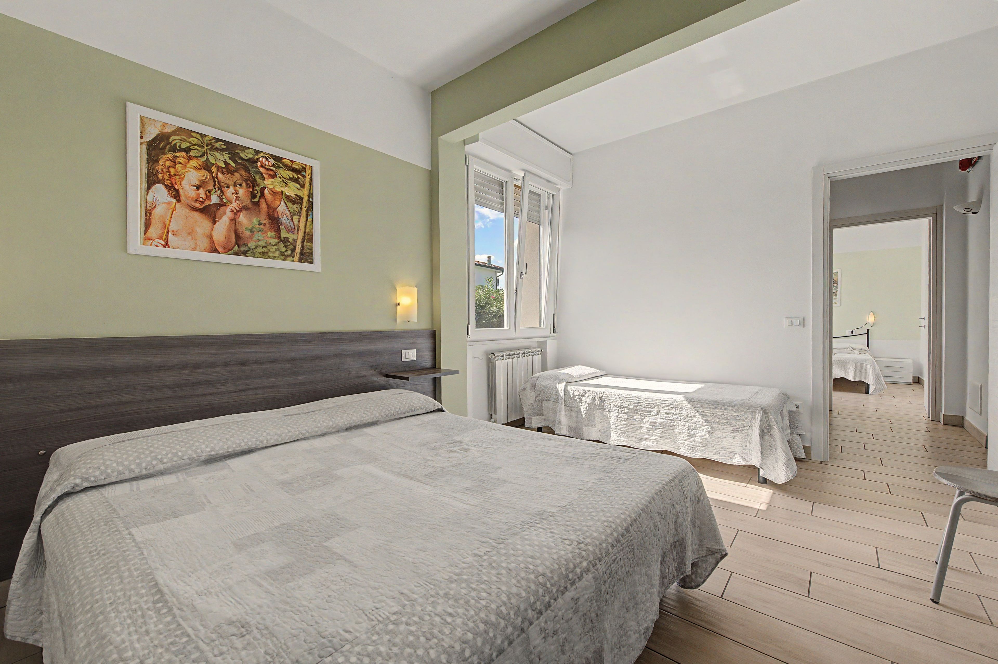 Ein Schlafzimmer mit zwei Betten, einem Gemälde an der Wand und Blick auf einen anderen Raum durch eine geöffnete Tür.