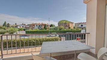 Un balcone con tavolo e sedie, affacciato su una zona residenziale con case e una strada.