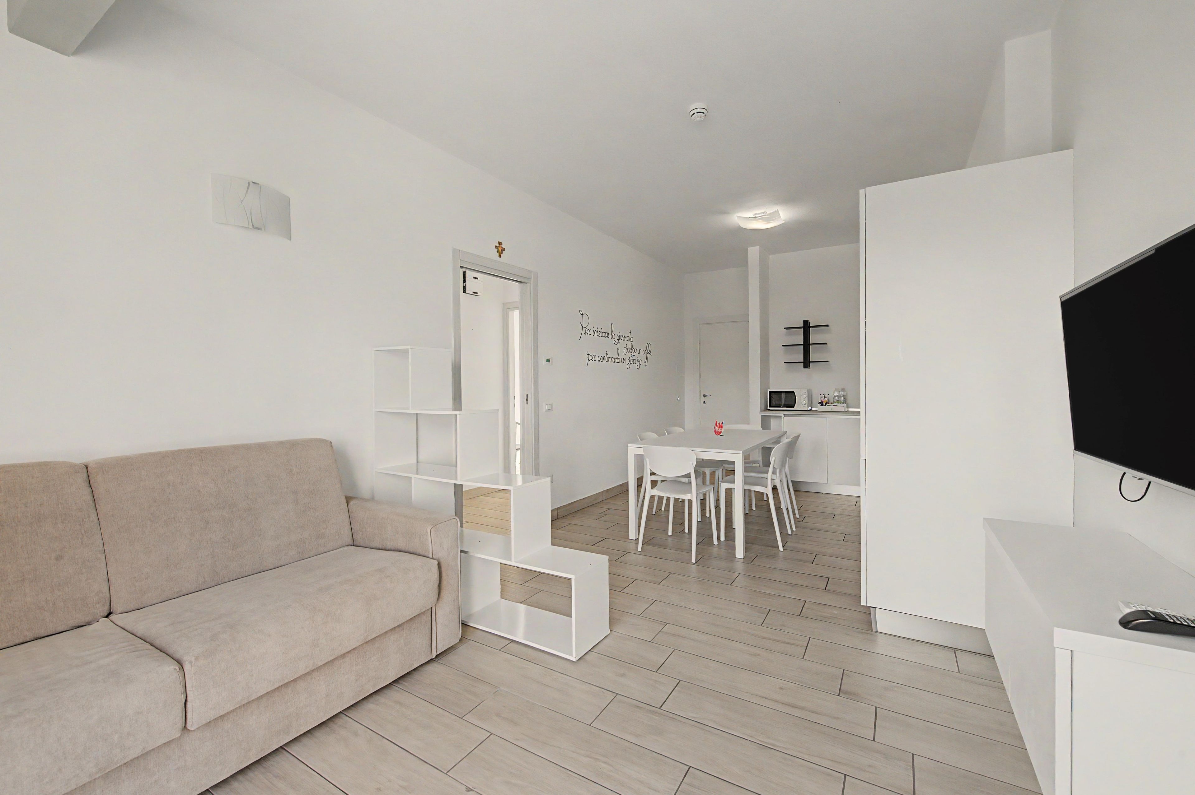 Ein modernes Wohnzimmer mit einer Couch, einem Esstisch mit Stühlen, einer Küchenzeile und einem an der Wand befestigten Fernseher.