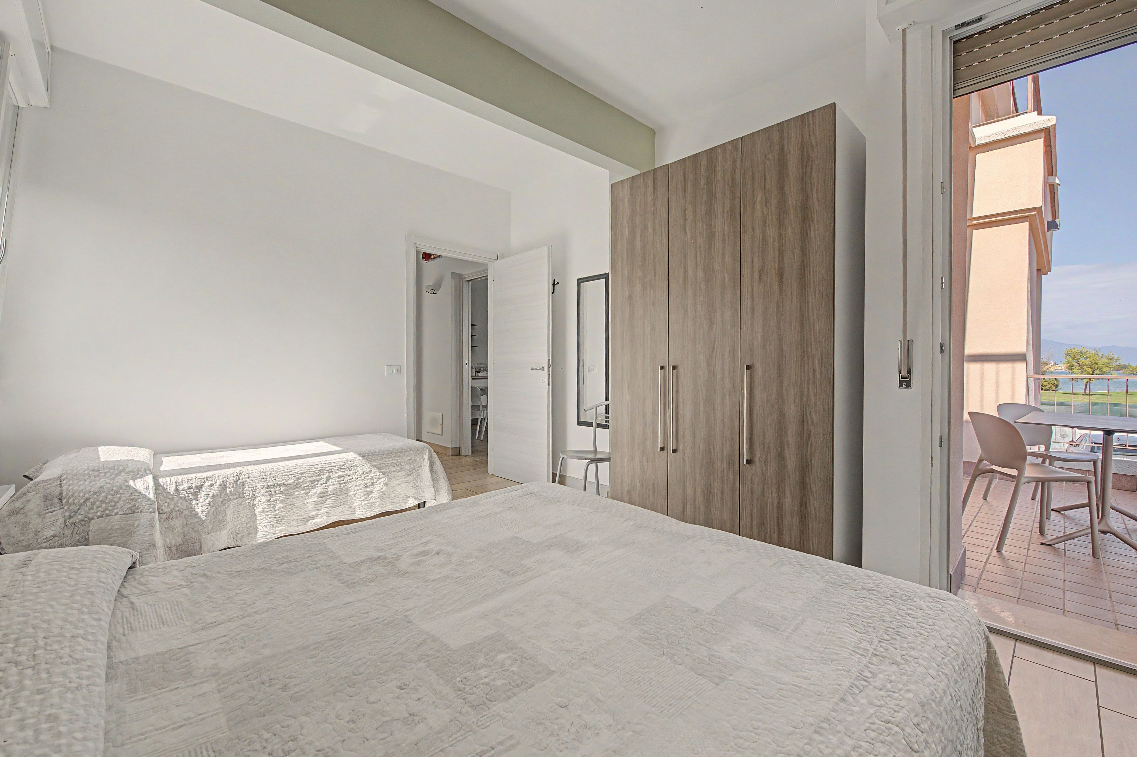 Une chambre dotée d’une grande armoire, d’un lit recouvert d’une couvre-lit à motifs et offrant une vue sur un balcon aménagé avec du mobilier d’extérieur.