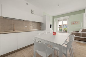A modern kitchen with white cabinets, a built-in oven, and a dining area with a white table and chairs. - 'Calla - Trilocale Deluxe' Apartment with Lake View, Wi-Fi and Air Conditioning (Sirmione)