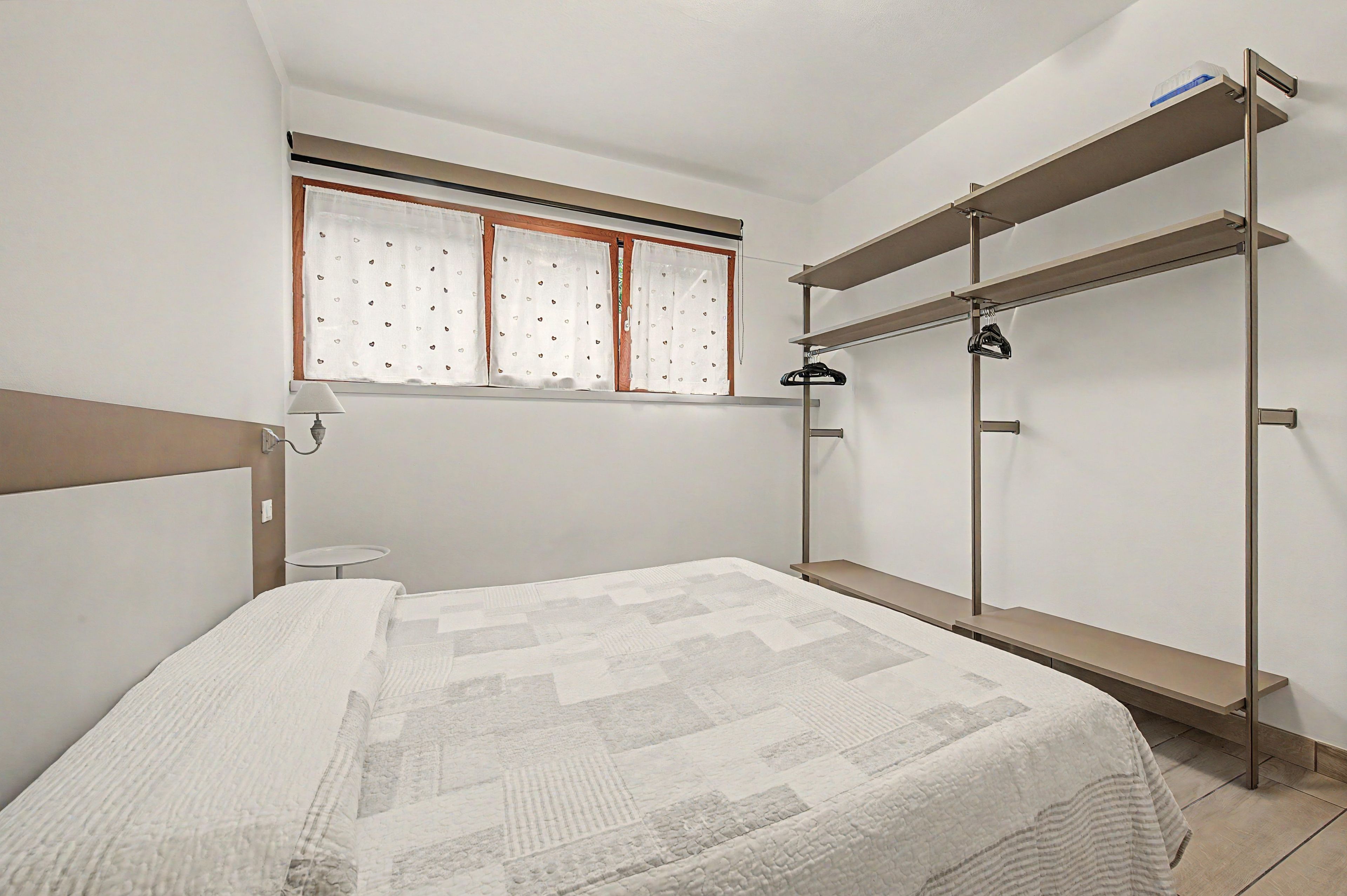 Un dormitorio con cama, ventana con cortinas, mesita de noche y armario empotrado.