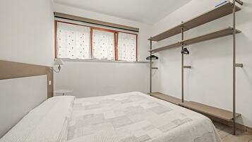 Un dormitorio con cama, ventana con cortinas, mesita de noche y armario empotrado.