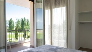 Ein Zimmer mit einer großen Schiebeglasdoor zum Balkon mit Blick auf Bäume und eine Rasenfläche.
