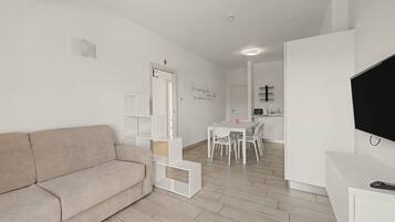 Ein modernes Wohnzimmer mit einer Couch, einem Esstisch mit Stühlen, einer Küchenzeile und einem an der Wand befestigten Fernseher.