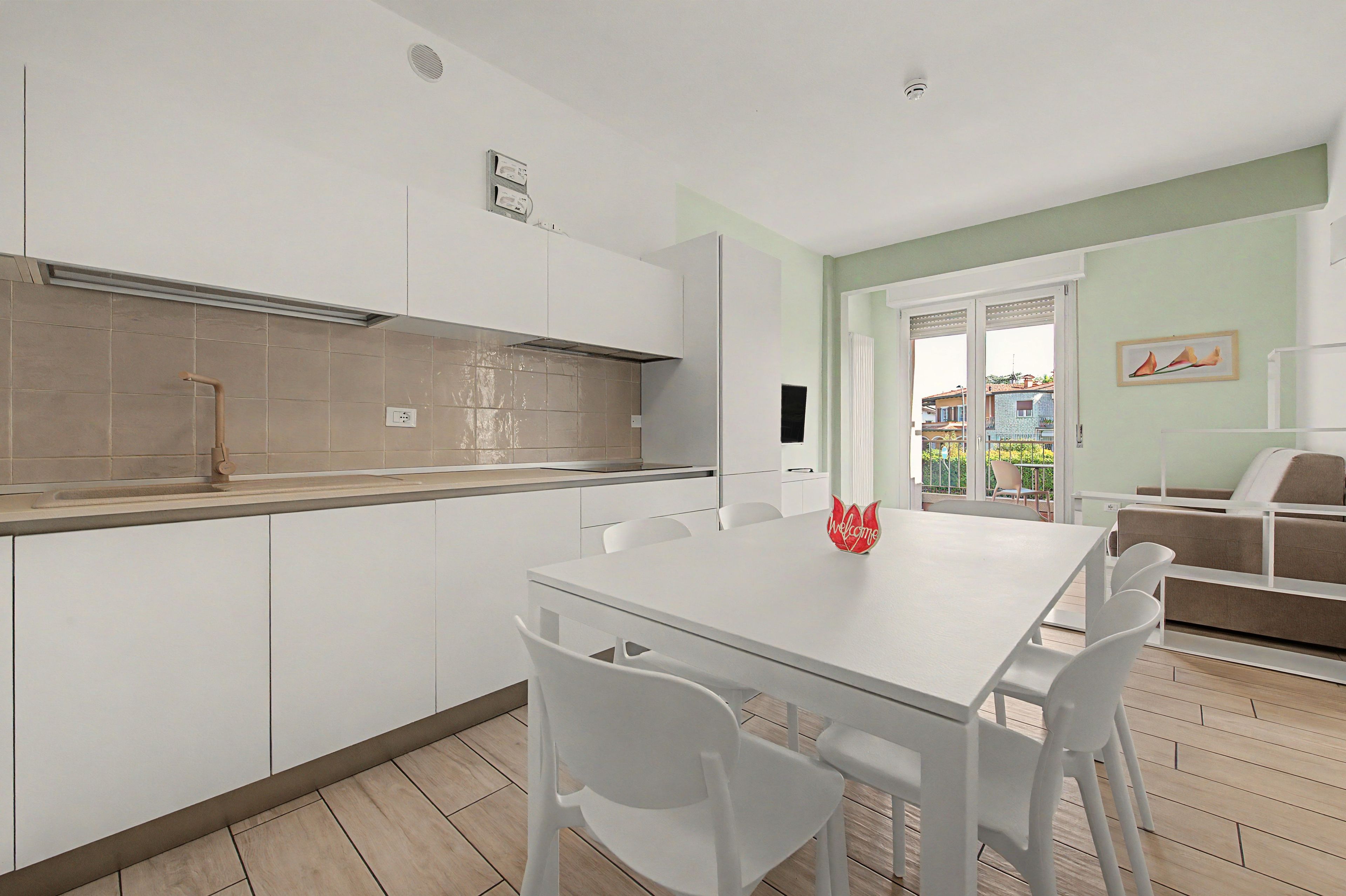 Eine moderne Küche mit weißen Schränken, einem eingebauten Backofen und einem Essbereich mit einem weißen Tisch und Stühlen.