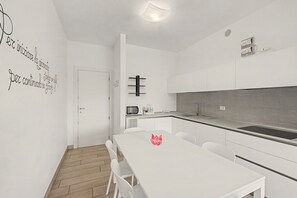 A modern kitchen with white cabinetry, a microwave, and a sink. There is a dining table with chairs and a 'Welcome' sign on it. - 'Calla - Trilocale Deluxe' Apartment with Lake View, Wi-Fi and Air Conditioning (Sirmione)