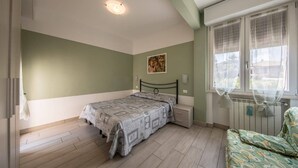 Ein Schlafzimmer mit einem Bett, einem Nachttisch, einem Fenster mit Vorhängen und einer Heizung.