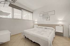 A modern bedroom with a bed, a bedside table, a mirror, and a window with curtains. - Ortensia Apartment - Economy Three-Room with Shared Pool, Wi-Fi, and Air Conditioning (Sirmione)