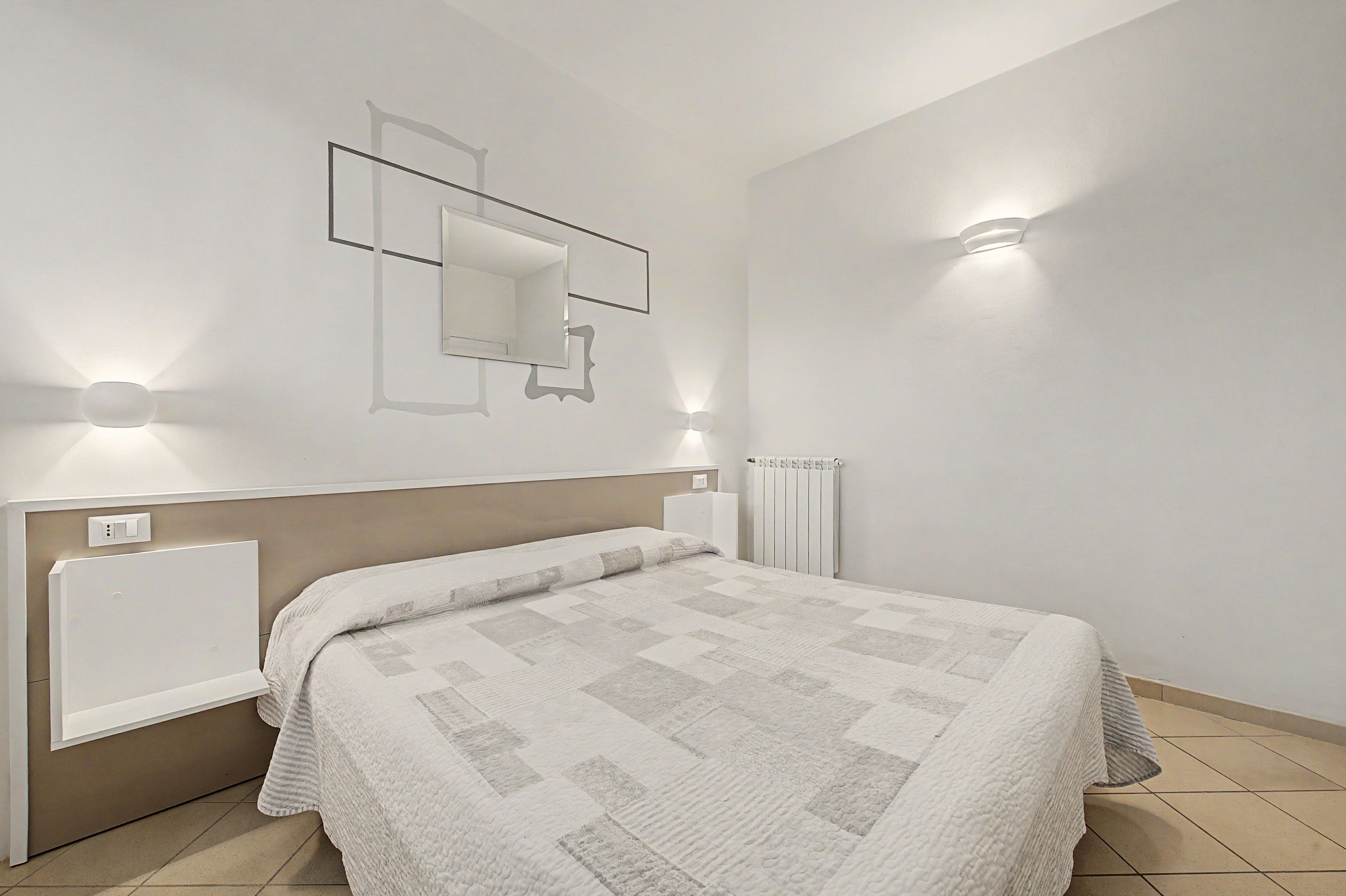 Ein Schlafzimmer mit einem Bett, einem Wandspiegel und zwei Wandleuchten.