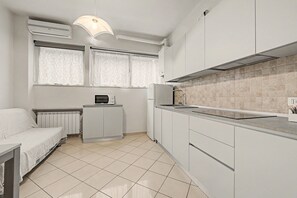 A compact kitchen with white cabinetry, a microwave, a kettle, and a small dining table. - Ortensia Apartment - Economy Three-Room with Shared Pool, Wi-Fi, and Air Conditioning (Sirmione)