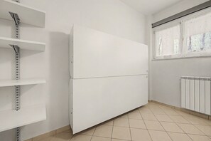 A room with a white wall, a window with a view, and a radiator. - Ortensia Apartment - Economy Three-Room with Shared Pool, Wi-Fi, and Air Conditioning (Sirmione)