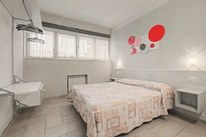 Ein Schlafzimmer mit einem Bett, einem Schreibtisch, einem Heizkörper und einer Wandleuchte.