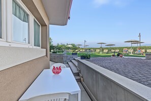 Ein Balkon mit einem weißen Tisch, einem roten Schild mit der Aufschrift 'Welcome' und Gartenmöbeln mit Sonnenschirmen.