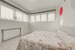 Een slaapkamer met een bed, een radiator en ramen met stippen gordijnen.