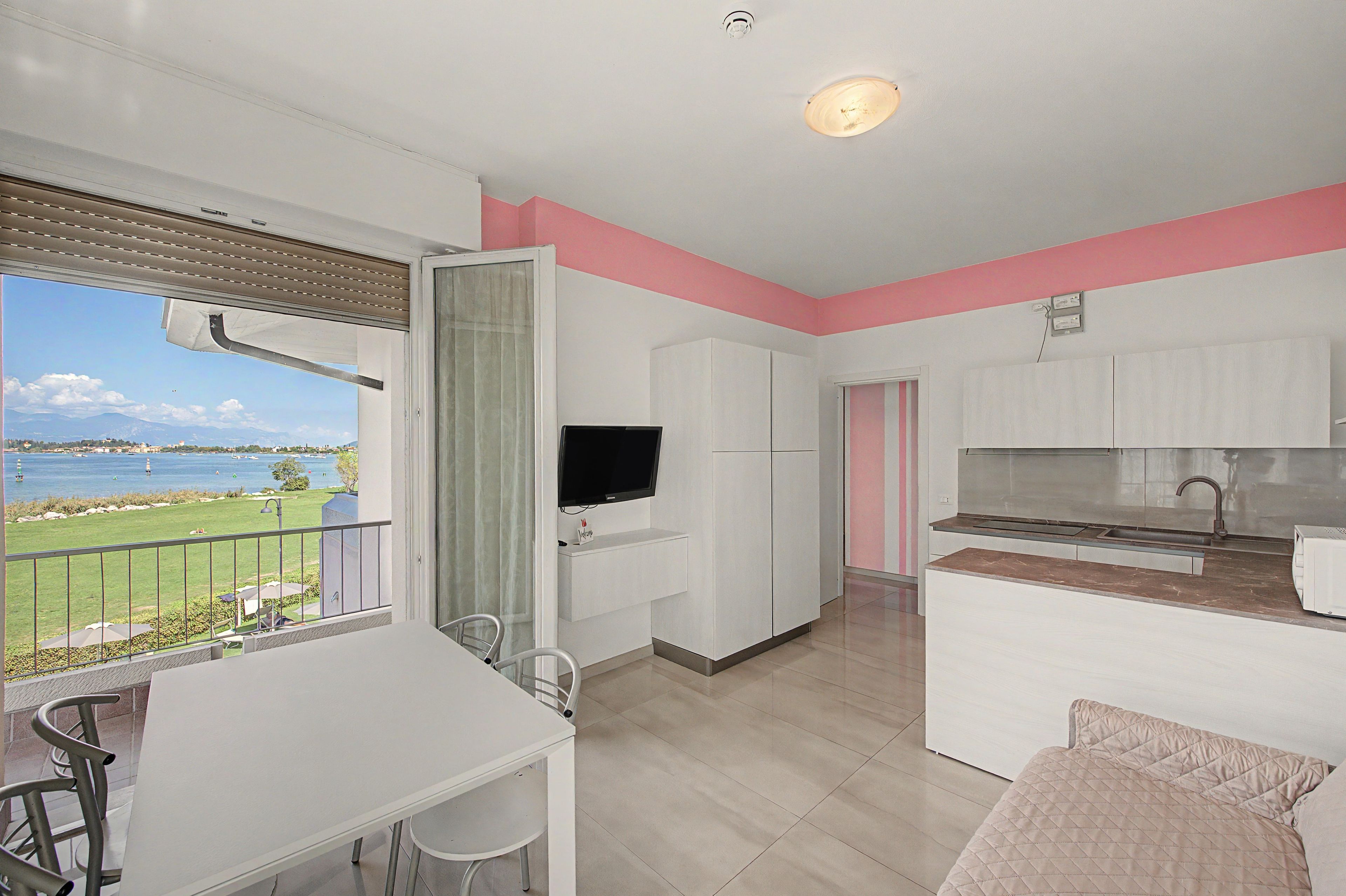 Eine moderne Küche mit Flachbildfernseher, ein Essbereich mit Tisch und Stühlen sowie Blick auf ein Gewässer vom Balkon aus.