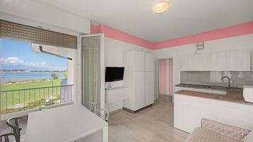 Eine moderne Küche mit Flachbildfernseher, ein Essbereich mit Tisch und Stühlen sowie Blick auf ein Gewässer vom Balkon aus.